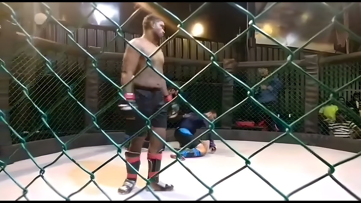 A fighter standing over his opponent inside an outdoor cage at night