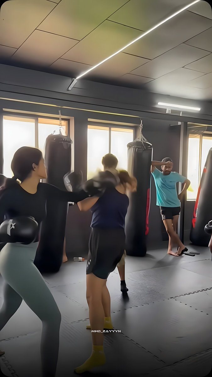 Women practising boxing on the gym floor beside the heavy bags