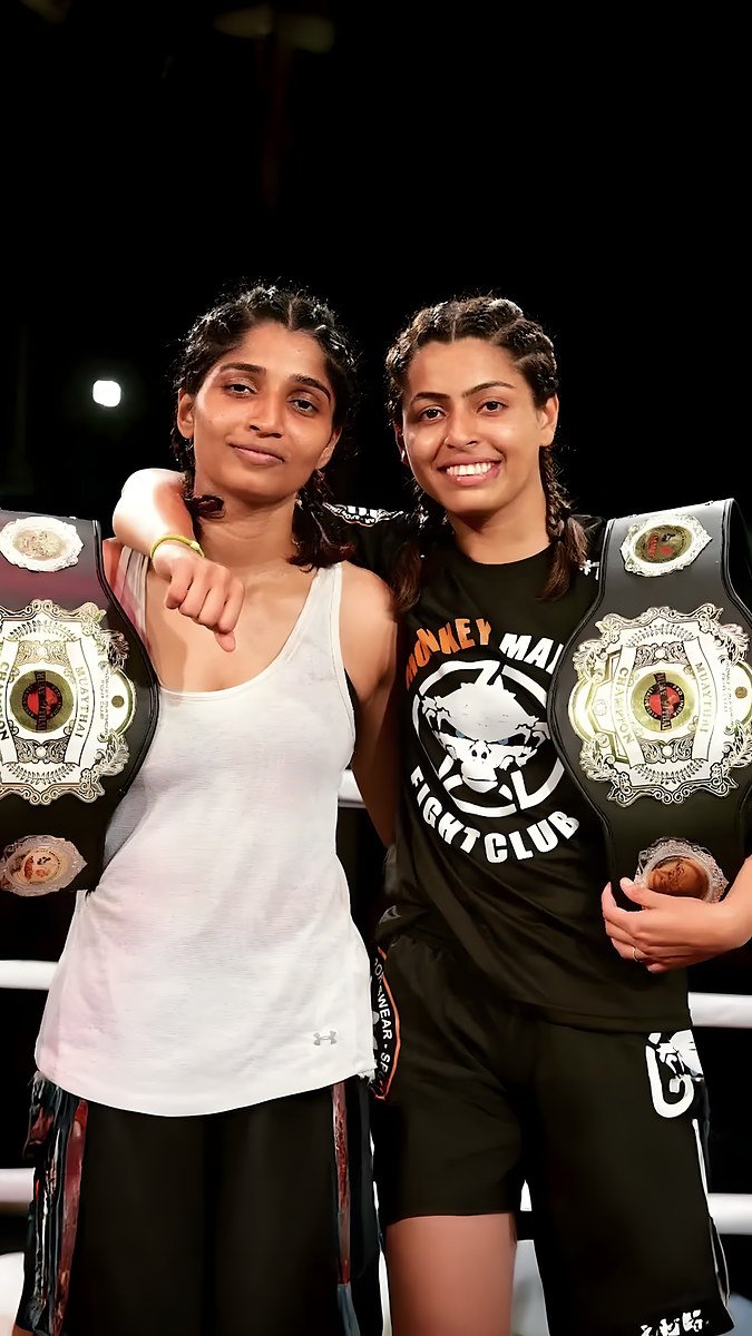 Two women fighters in a ring holding championship belts, one in a Monkey Mayhem Fight Club vest