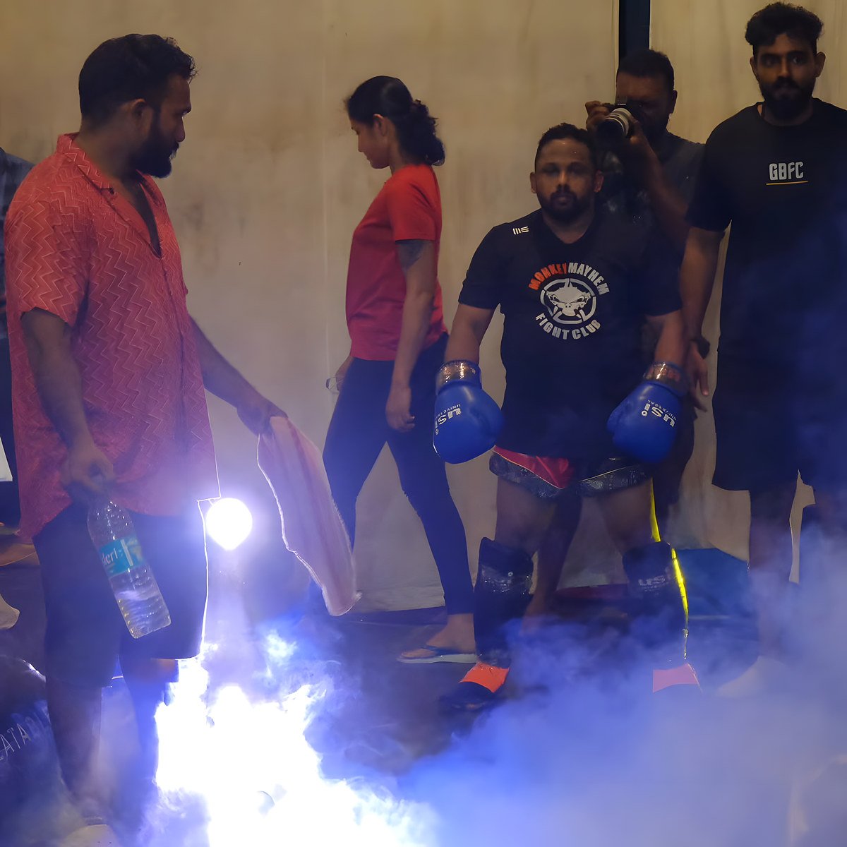 A fighter in gloves walking out through stage smoke with his corner team