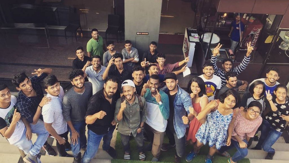 Overhead group photo of about thirty smiling members throwing fists and peace signs in front of a building entrance.