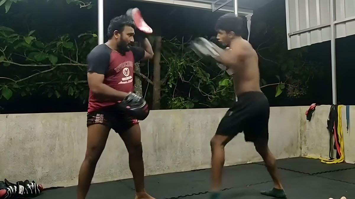 A coach holding pads as a trainee throws a kick in an outdoor training area